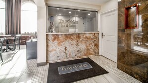 Zona de recepción con pared de mármol, mostrador de recepción y felpudo con el nombre del hotel.