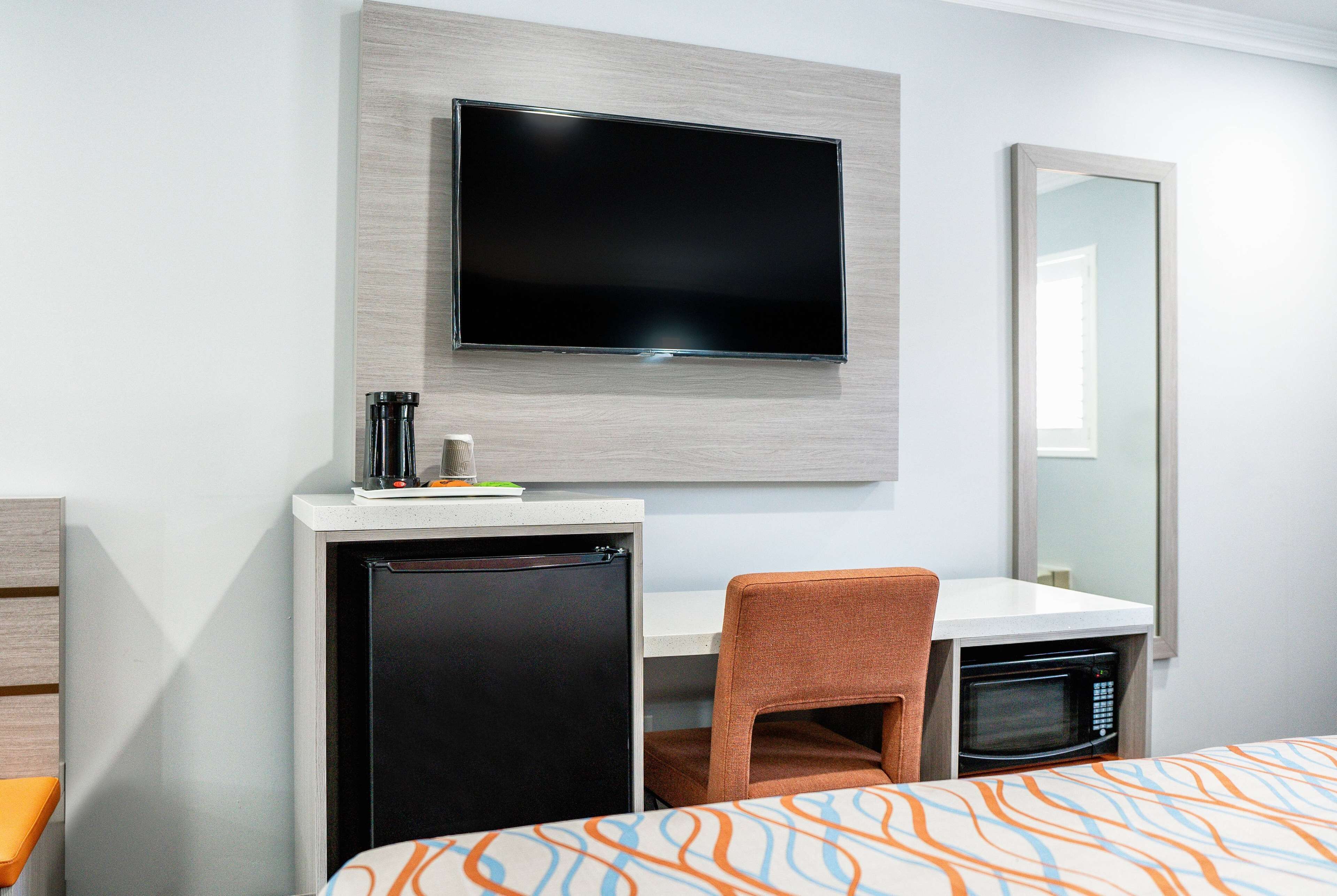 Une chambre d’hôtel équipée d’un lit, d’un bureau avec une chaise, d’une télévision, d’un four à micro-ondes et d’un réfrigérateur.