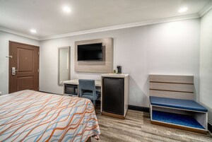 Habitación de hotel con cama, escritorio, silla, televisor y una pequeña zona de estar.