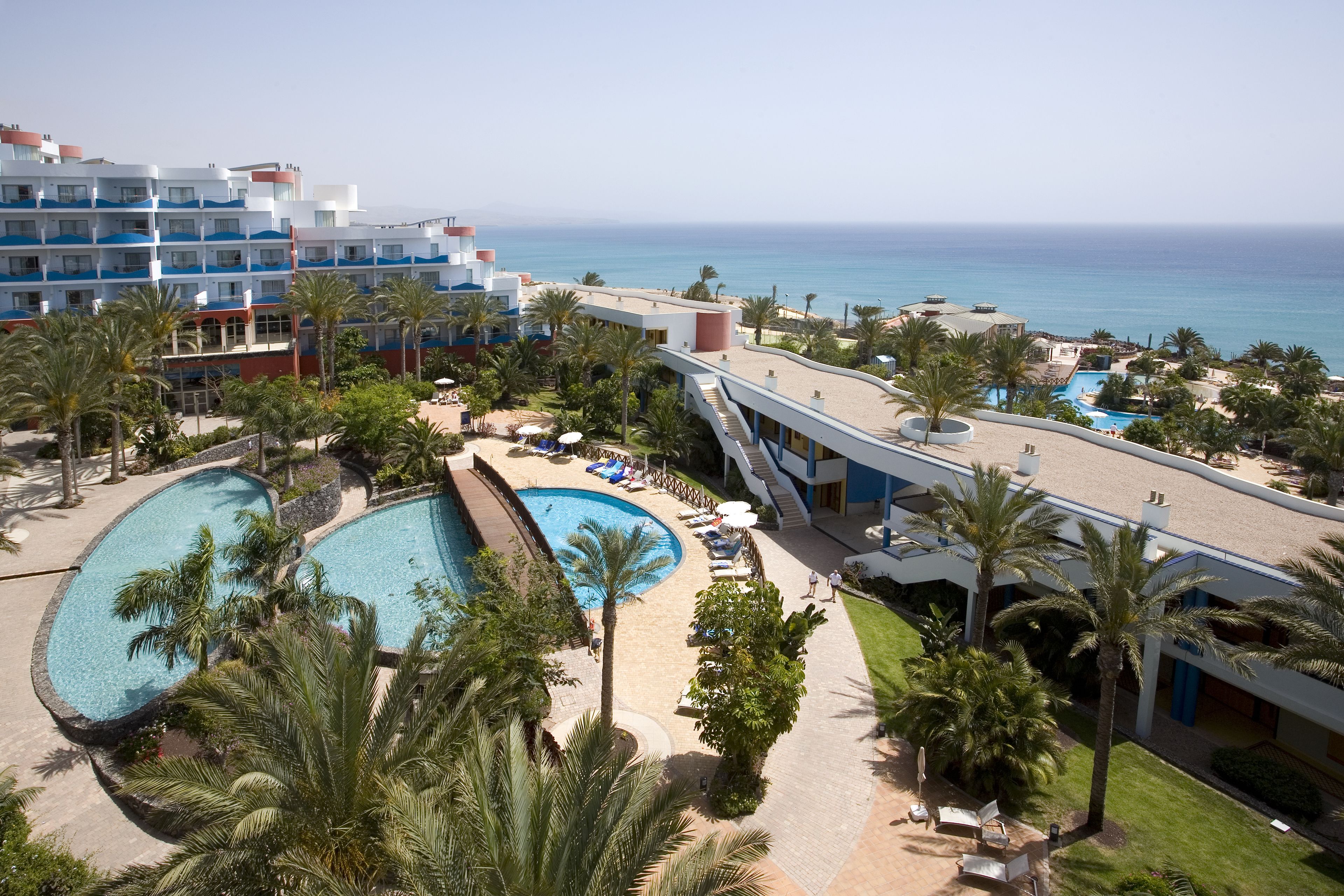 A resort with a large pool, palm trees, and a view of the ocean.