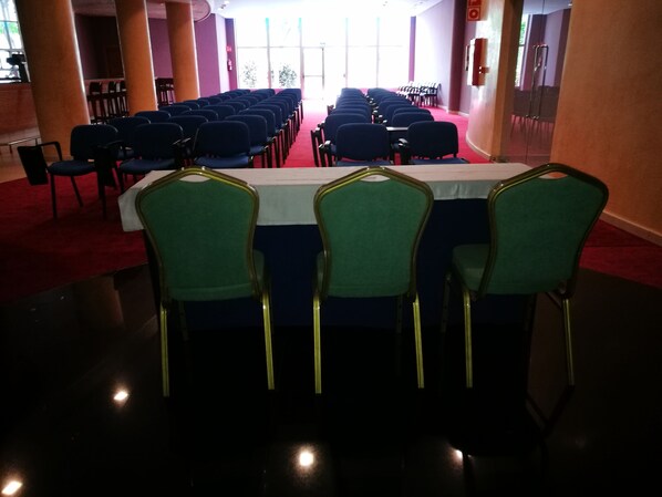 A conference room with rows of chairs and tables, large windows, and a red carpet.