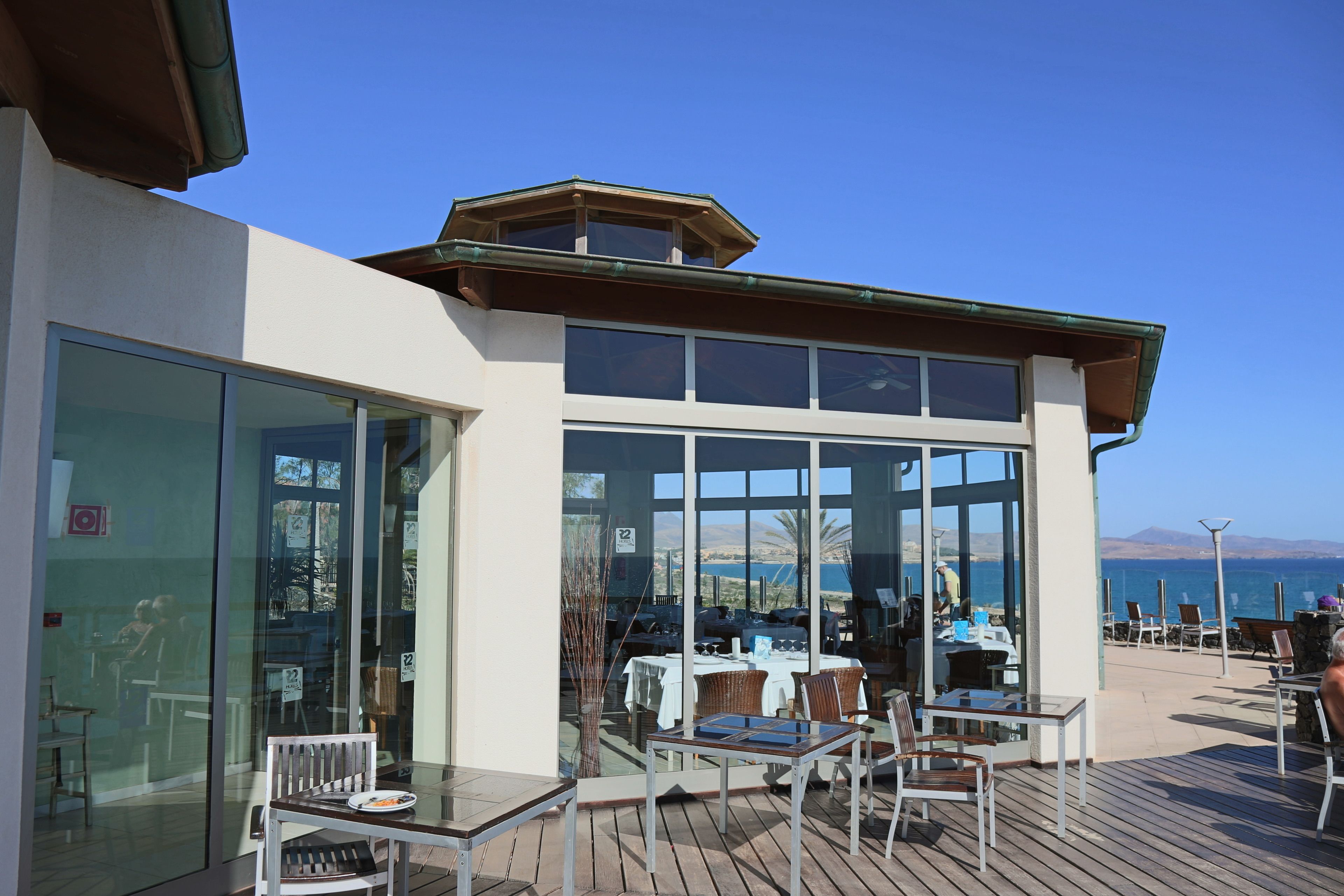 A modern outdoor dining area with glass walls, wooden deck, and tables and chairs.