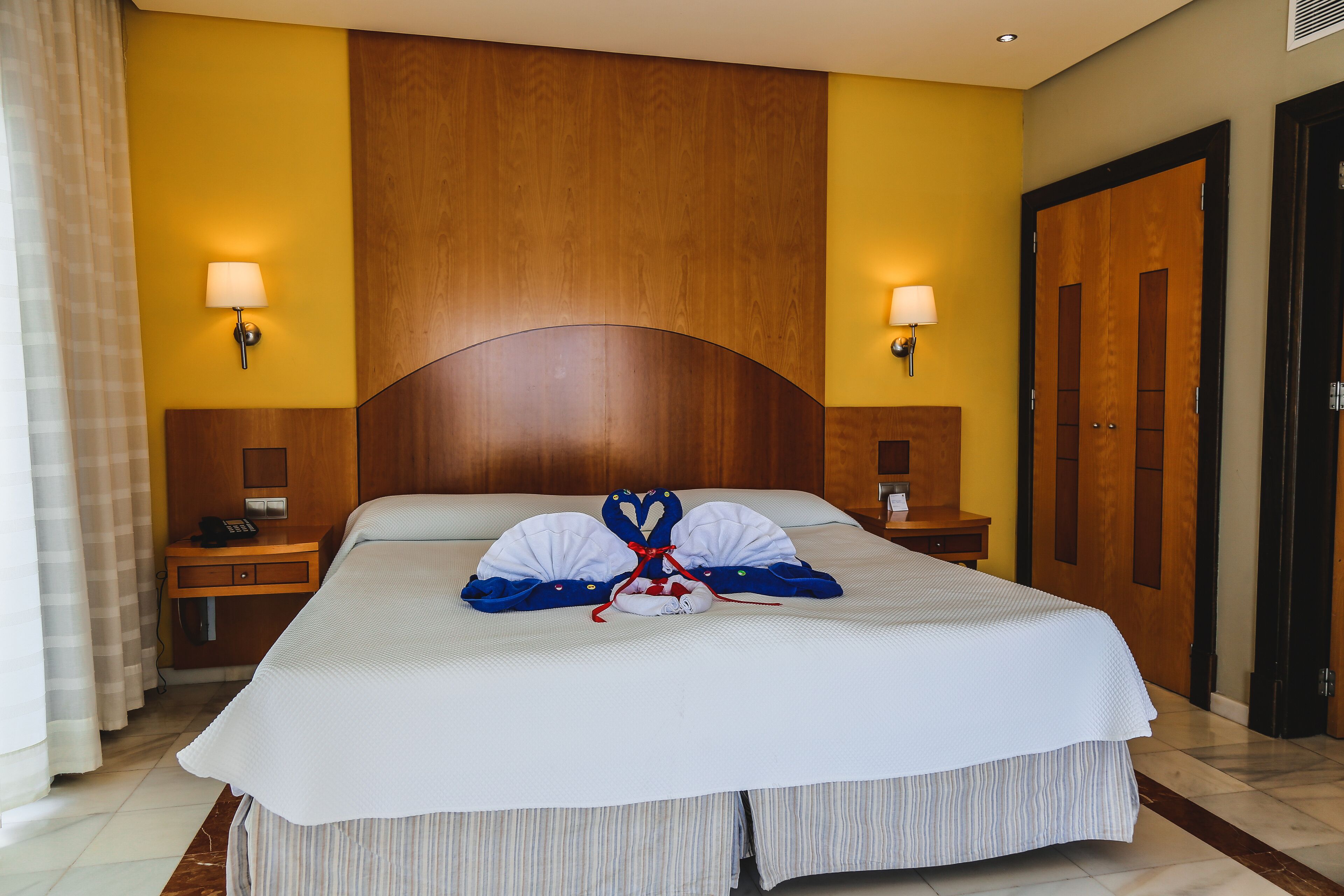 A hotel room with a large bed, wooden headboard, two bedside tables with lamps, and a door.