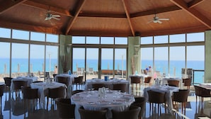 A restaurant with tables set for dining, large windows offering a view of the beach, and wooden ceiling beams. - R2 Pájara Beach Hotel & Spa - All Inclusive (Pajara)