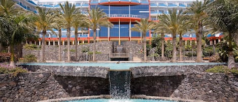 A hotel with a pool, palm trees, and a waterfall.