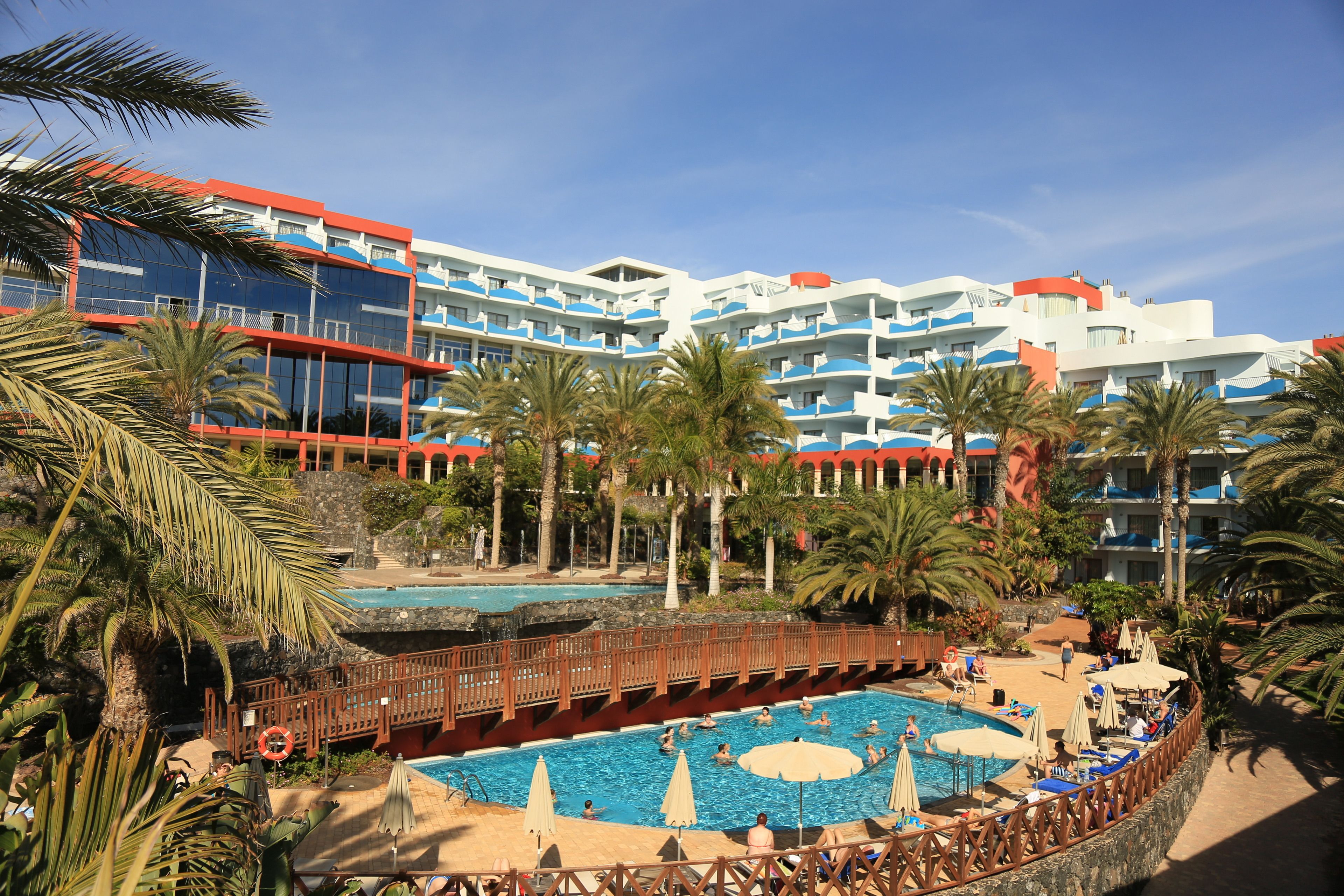 A resort with a central pool, multiple balconies, and palm trees.