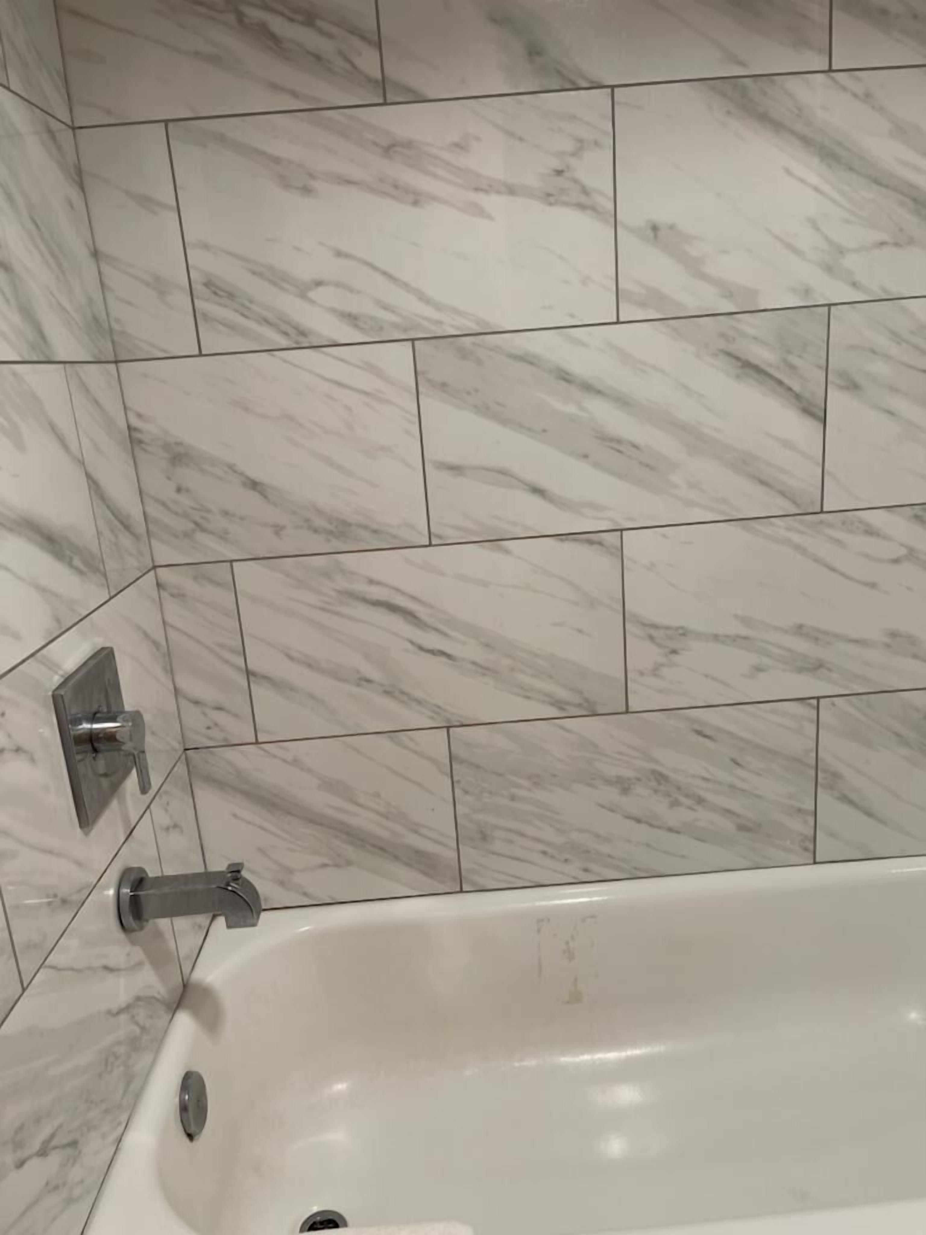 Une salle de bain avec une baignoire blanche, des carreaux de marbre et un robinet moderne.