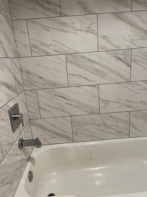 A bathroom with a white bathtub, marble tiles, and a modern faucet. - Bear Mount Inn & Suites (Pigeon Forge)