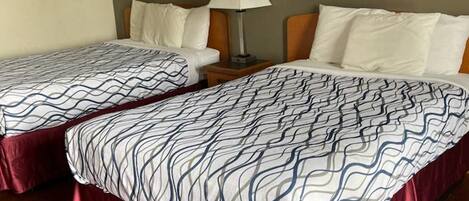 Habitación de hotel con dos camas, cada una con colcha estampada y patas cubiertas de tela roja. Hay una mesita de noche con una lámpara entre las camas, y dos cuadros enmarcados en la pared.