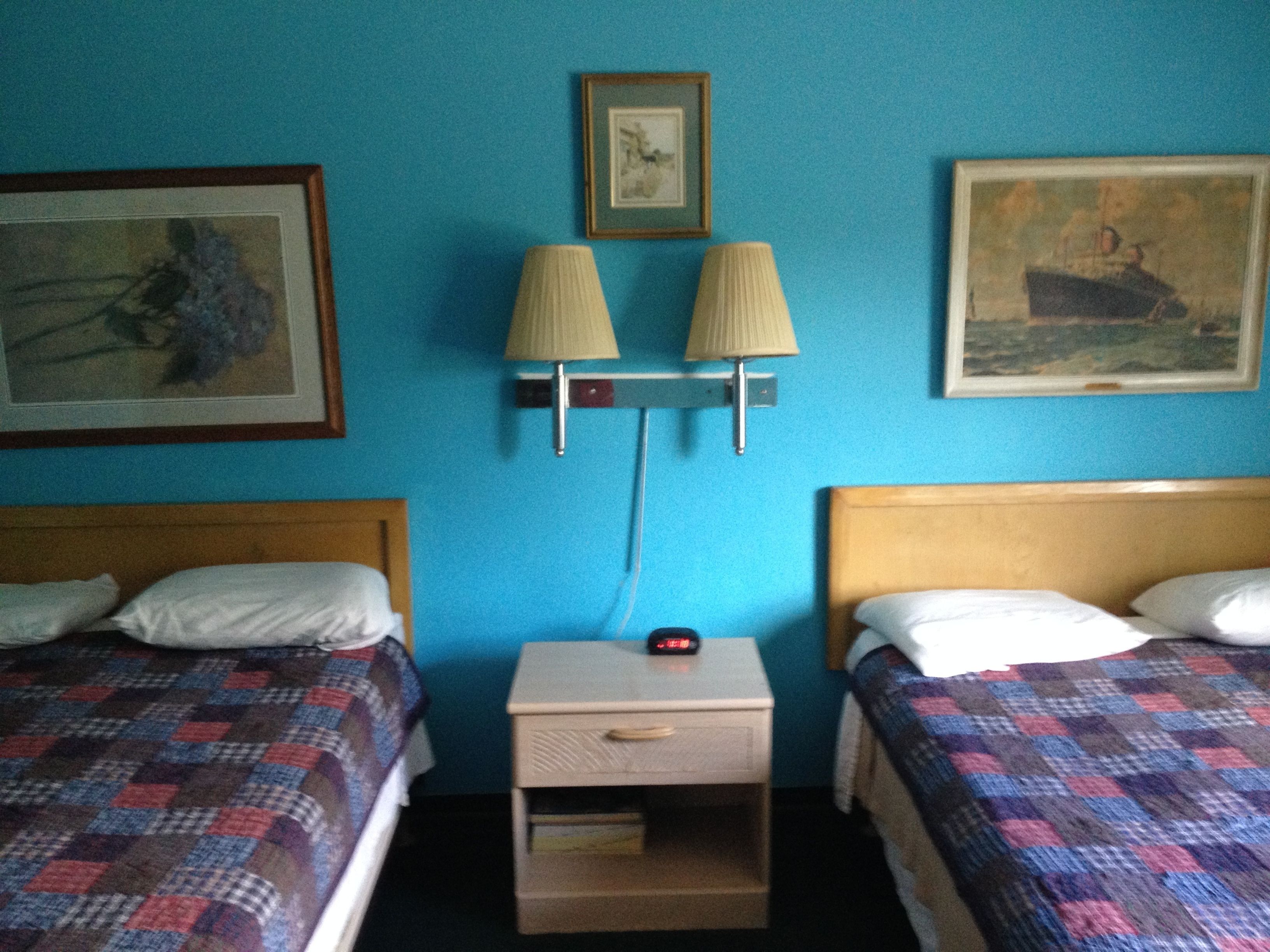 A hotel room with two beds, a nightstand with a lamp, and two framed pictures on the wall.