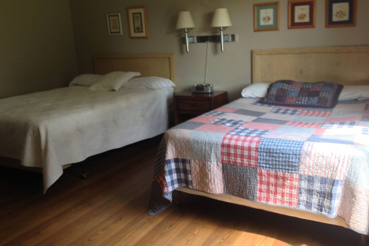 Un dormitorio con dos camas, suelo de madera, lámparas de noche y cuadros en la pared.