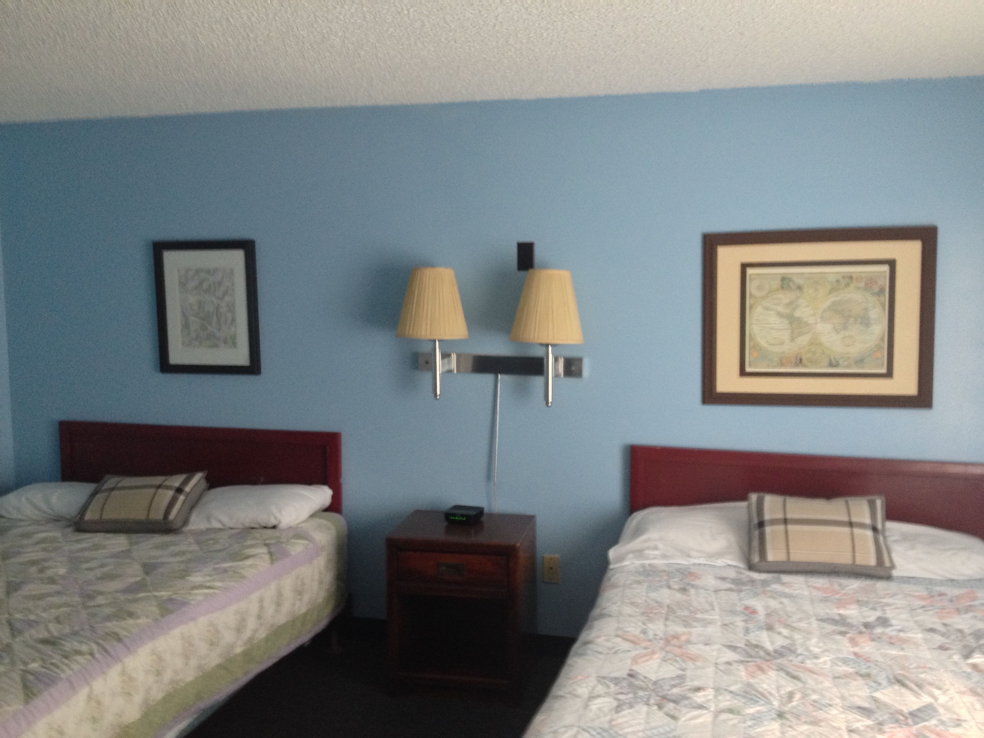 A hotel room with two beds, a nightstand, two wall-mounted lamps, and two framed pictures.