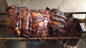 A large, roasted pig on a spit over a metal tray. - Chaffee Lodge (Chaffee)