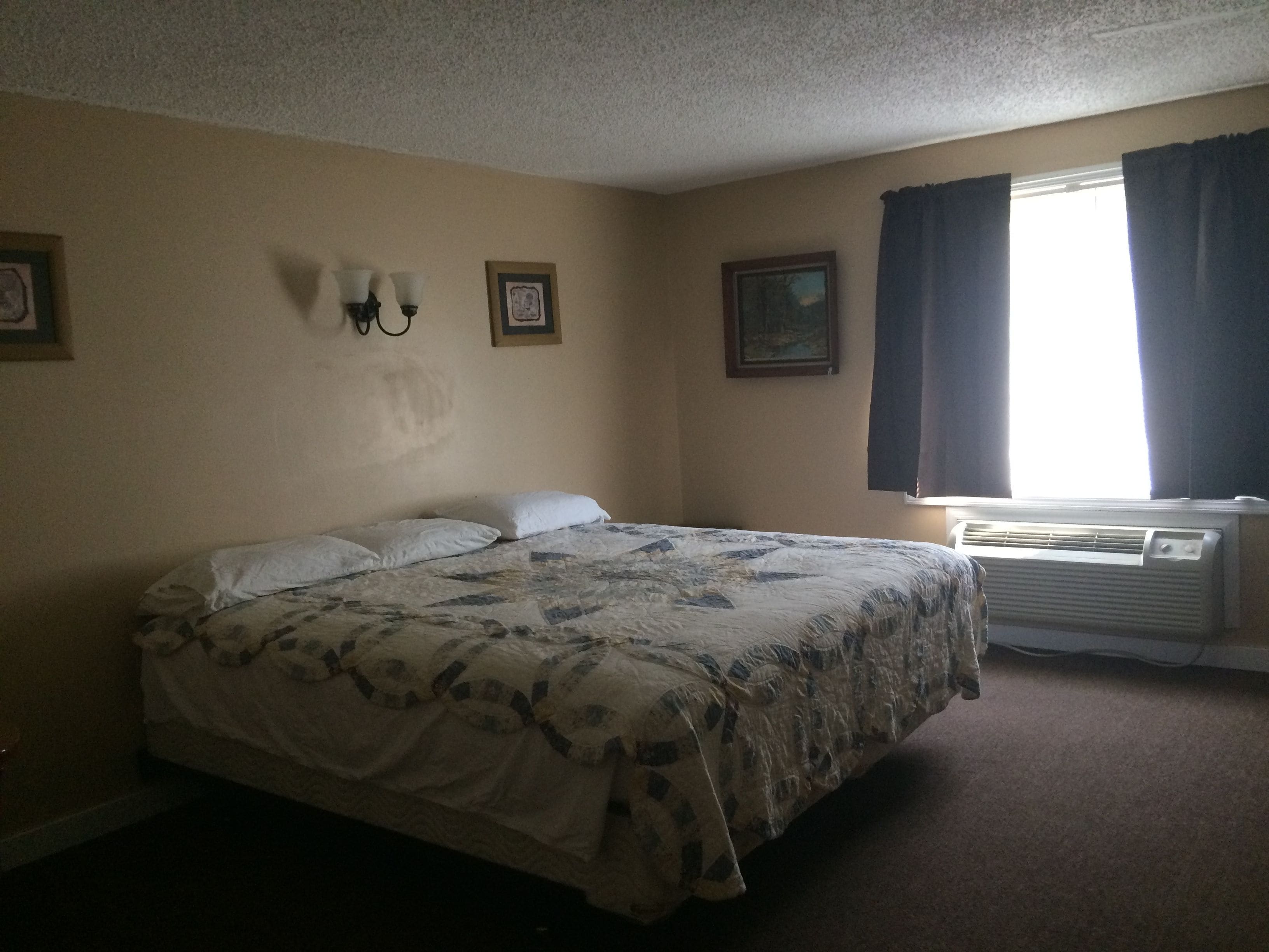 A bedroom with a bed, two wall-mounted light fixtures, a window with curtains, and an air conditioning unit.