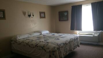A bedroom with a bed, two wall-mounted light fixtures, a window with curtains, and an air conditioning unit.