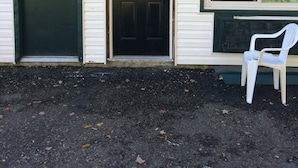 A house with a dark green door marked with the number 8, a front door with a window, and a white plastic chair outside. - Chaffee Lodge (Chaffee)