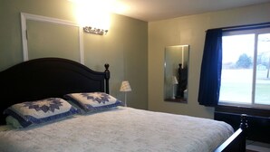 A bedroom with a bed, a nightstand, a lamp, a mirror, and a window with curtains. - Chaffee Lodge (Chaffee)