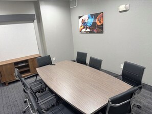 A conference room with a long table, black chairs, a wooden cabinet, and a wall-mounted painting. - Lubbock West Inn & Suites (Lubbock)
