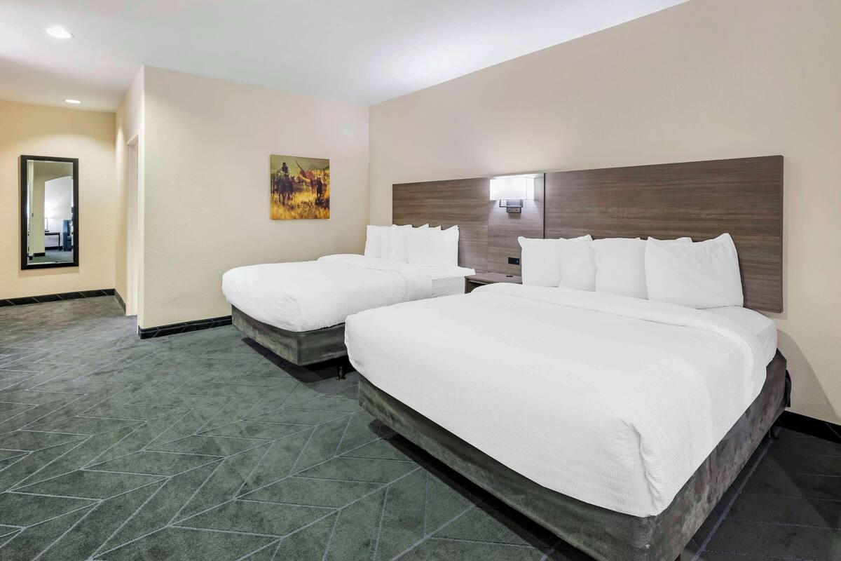 A hotel room with two beds, a large mirror, and a painting on the wall.