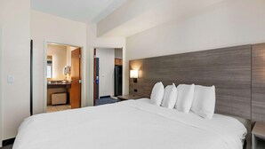 Habitación de hotel con una cama grande, cabecera de madera, mesita de noche y baño a la vista a través de una puerta abierta.
