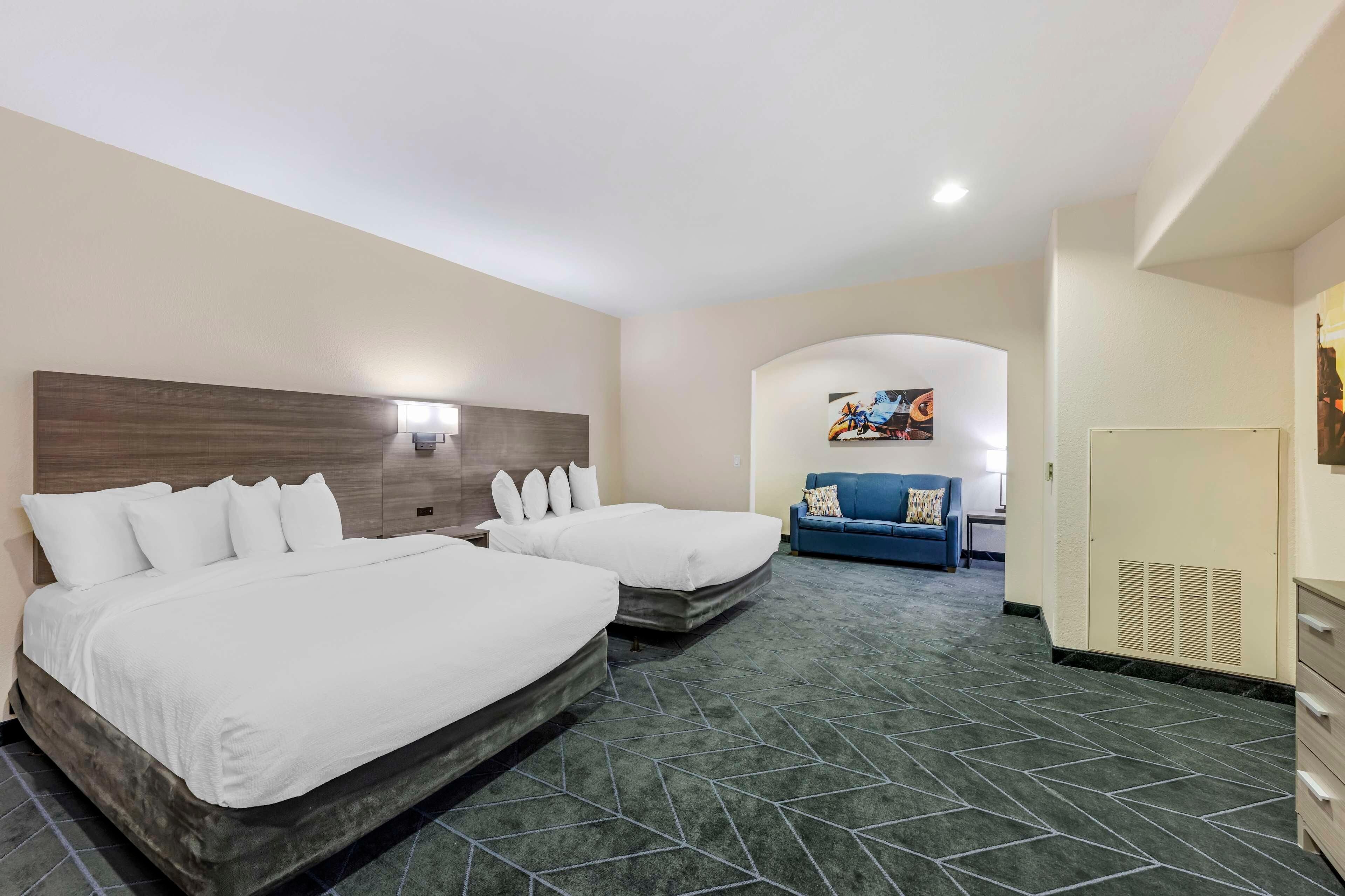 Une chambre d’hôtel avec deux lits, un canapé bleu, un tableau au mur et une armoire.