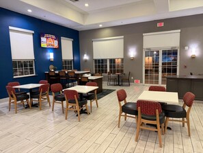 A restaurant with multiple tables and chairs, a blue accent wall, and an exit sign. - Lubbock West Inn & Suites (Lubbock)