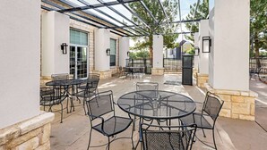 Un patio al aire libre con mesas y sillas redondas, una estructura de pérgola y un muro de piedra.