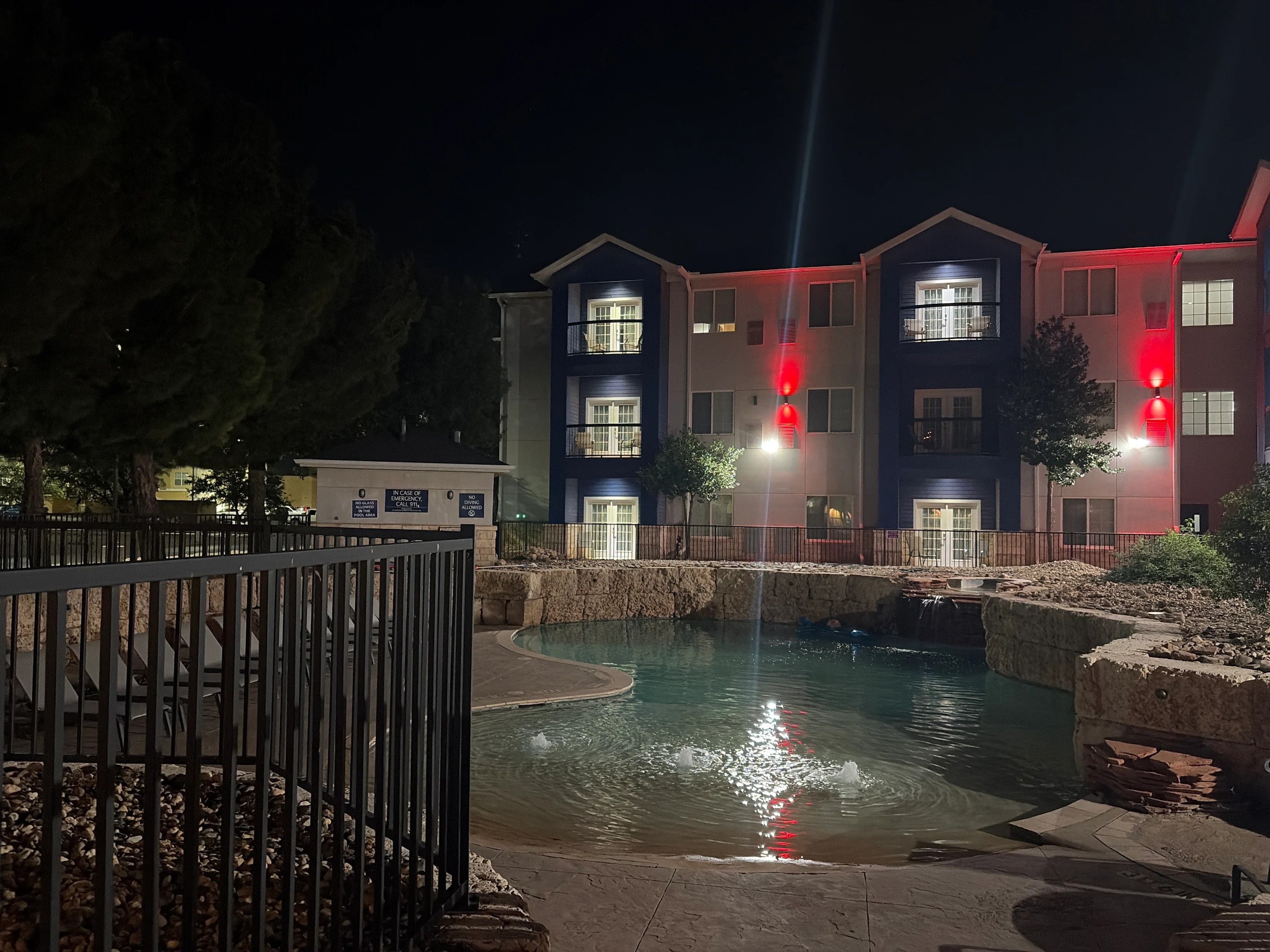 A nighttime view of a multi-story building with a swimming pool in the foreground.