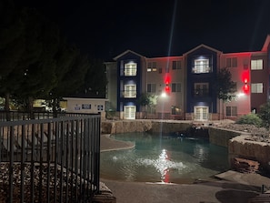 Vista nocturna de un edificio de varios pisos con una piscina en primer plano.