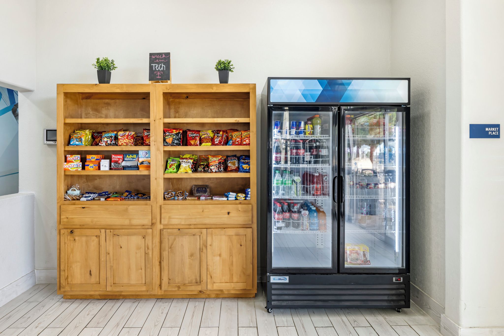 A kitchenette with a wooden cabinet stocked with snacks and a black refrigerator with a glass door.