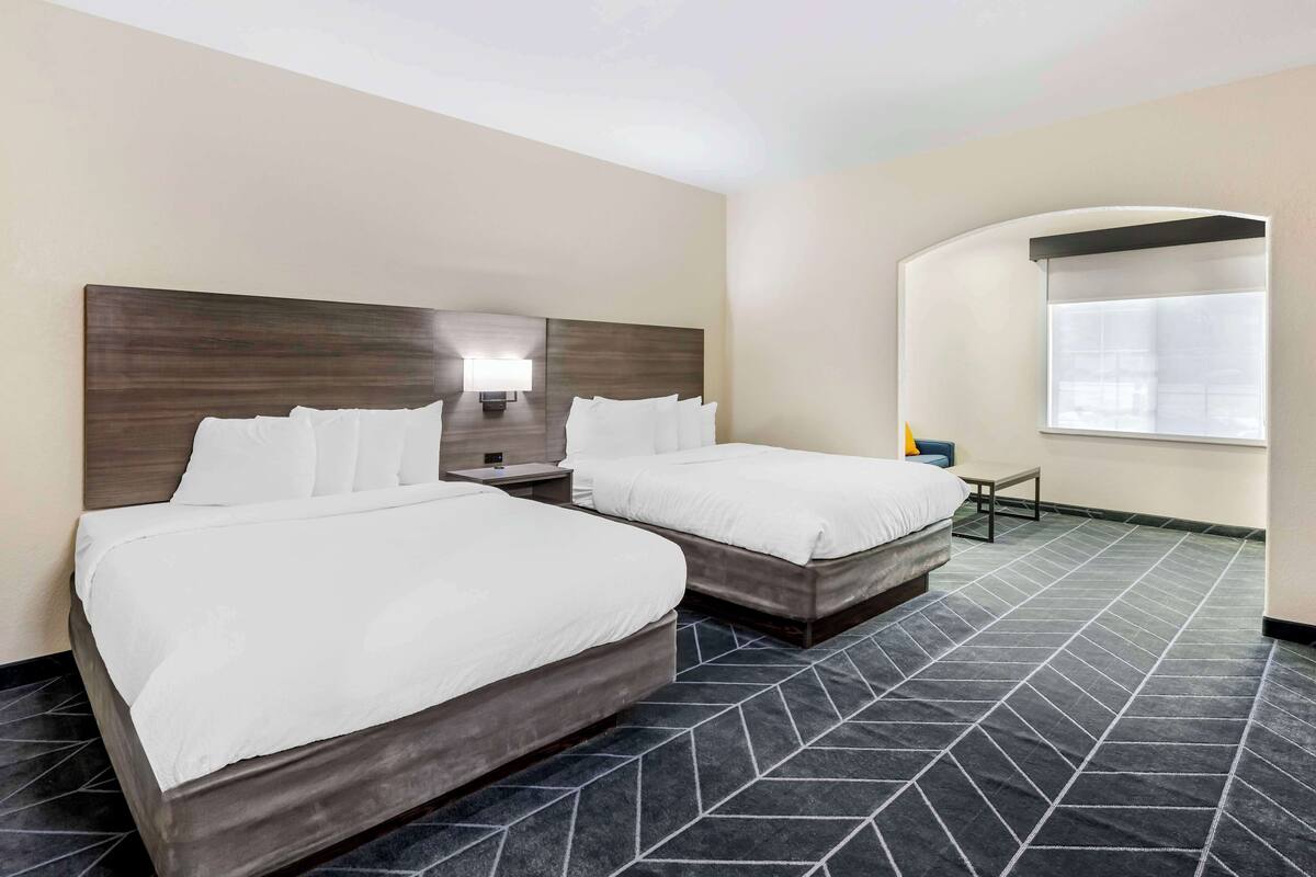 A hotel room with two beds, a nightstand with a lamp, a small table, and a window with a view.