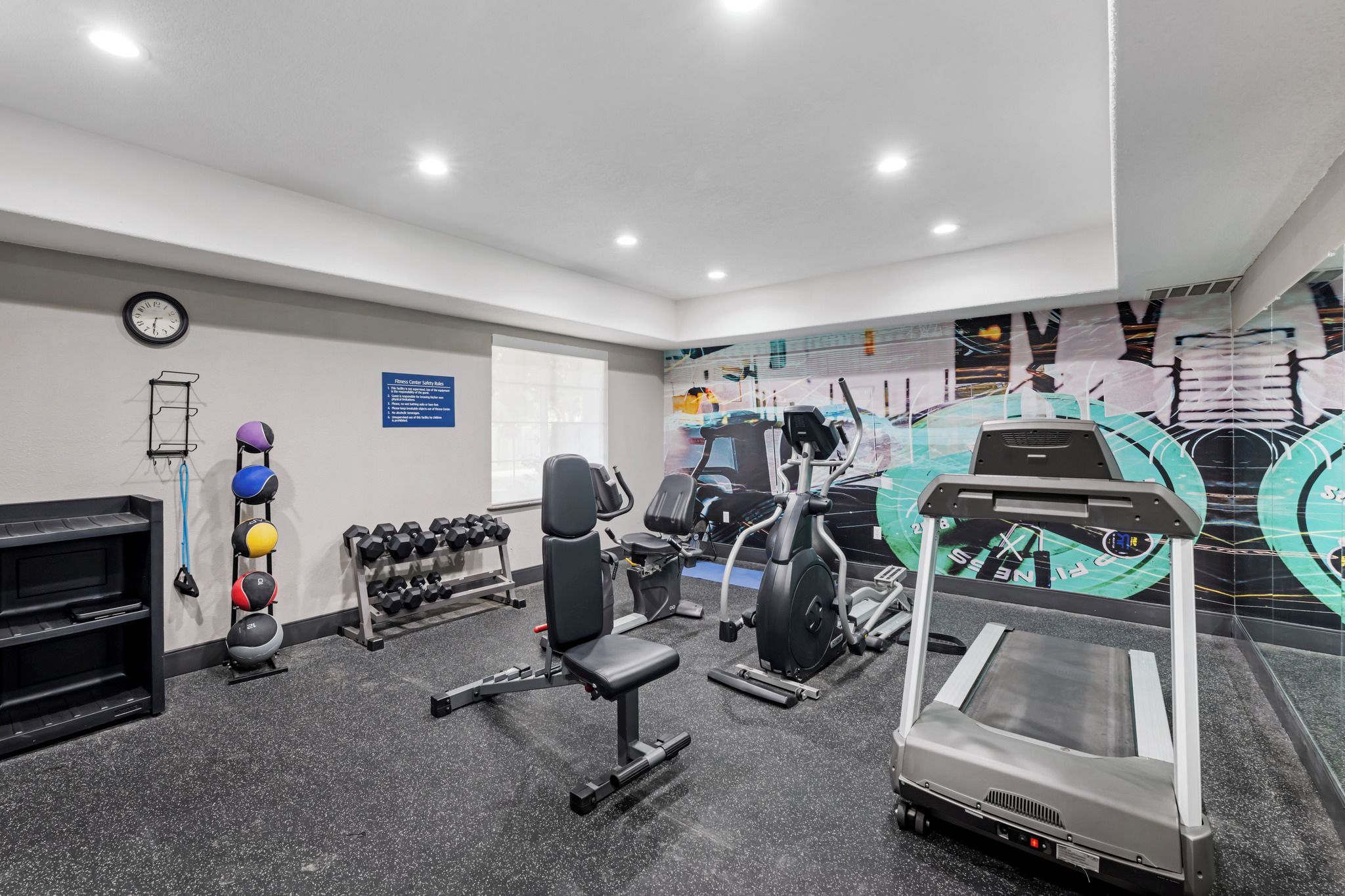 A gym with exercise equipment, a clock, and a sign with safety rules.