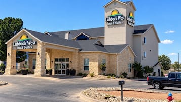 A Lubbock West Inn & Suites building with a stone facade, a prominent entrance, and a parking area with a fire hydrant.