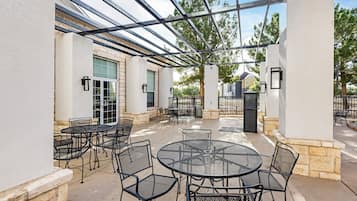 An outdoor patio with round tables and chairs, a pergola structure, and a stone wall.