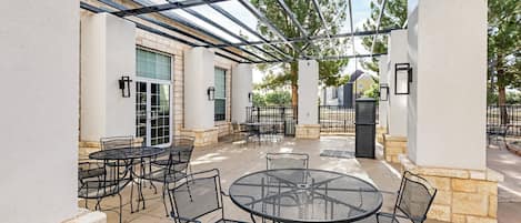 An outdoor patio with round tables and chairs, a pergola structure, and a stone wall.