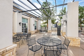 Une terrasse extérieure avec des tables et des chaises rondes, une structure en forme de pergola et un mur en pierre.
