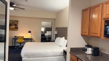Una habitación de hotel con una cama, un escritorio con una silla, una kitchenette y un ventilador de techo.