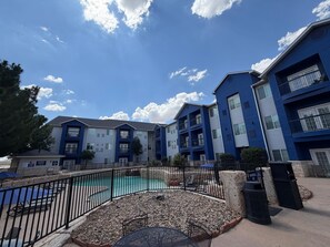 A residential building with a swimming pool, outdoor seating, and a clear sky.