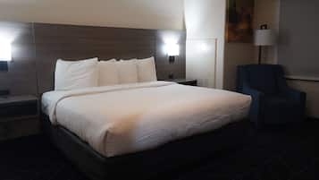 Una habitación de hotel con una cama grande, una silla, una mesita de noche y una lámpara fijada a la pared.