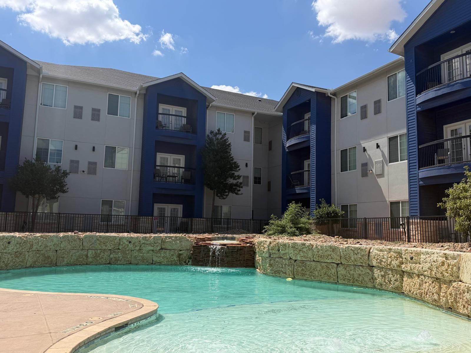 A residential building with multiple balconies, a swimming pool, and a stone wall.