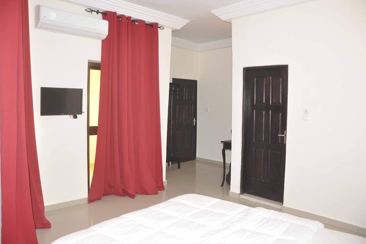 Habitación de hotel con cama, cortinas rojas, televisor de pantalla plana y dos puertas.