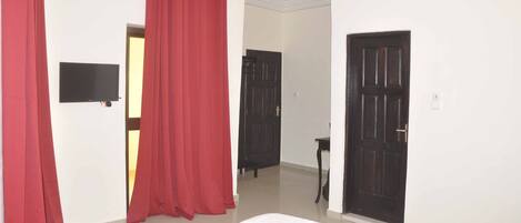 A hotel room with a bed, red curtains, a flat-screen TV, and two doors.