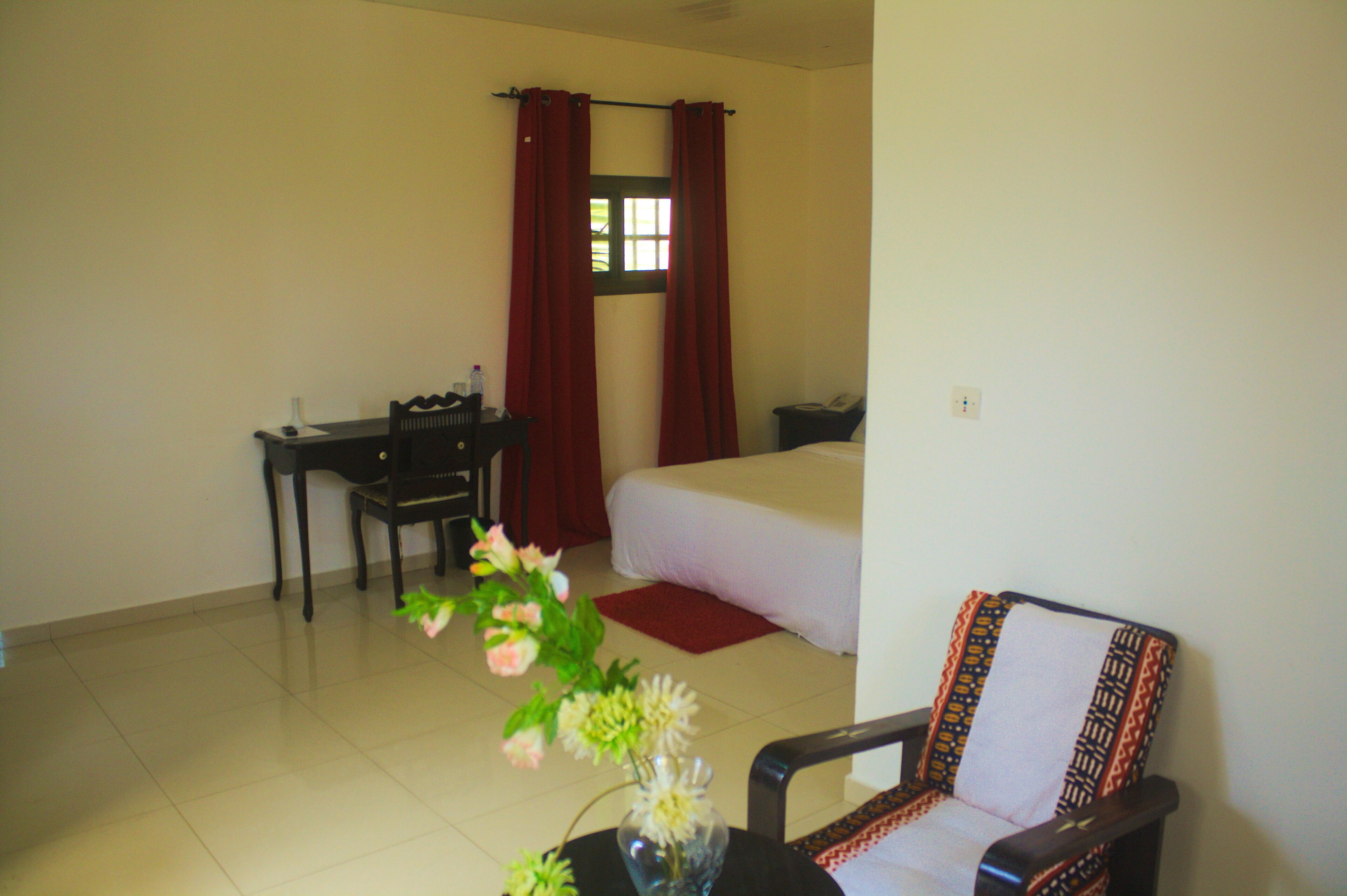 Une chambre d’hôtel avec un lit, un bureau, une chaise et un vase rempli de fleurs.
