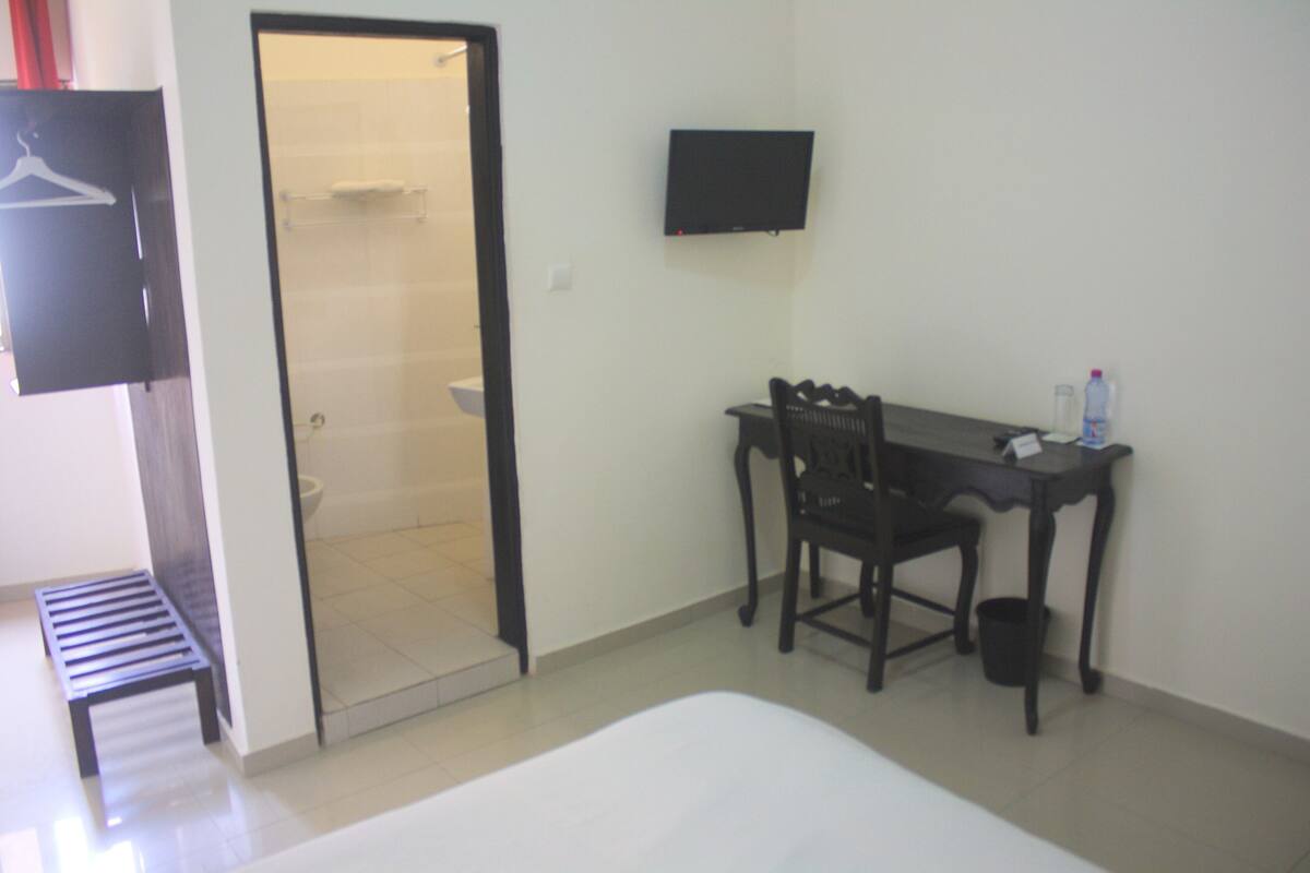 Habitación de hotel con cama, escritorio con silla, televisor en la pared y zona de ducha.