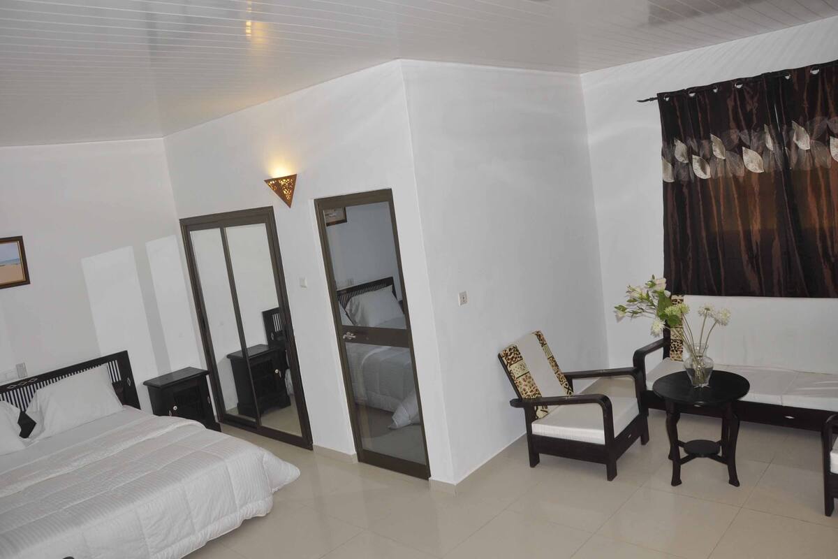 Habitación de hotel con cama, escritorio, silla, mesita, espejo y ventana con cortinas.