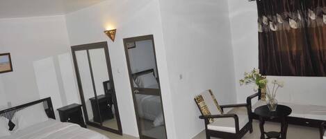 Habitación de hotel con cama, escritorio, silla, mesita, espejo y ventana con cortinas.
