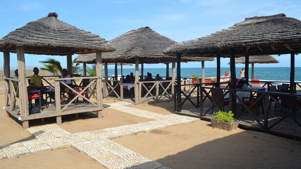Un restaurante frente a la playa con terraza techada de paja y vistas al océano.