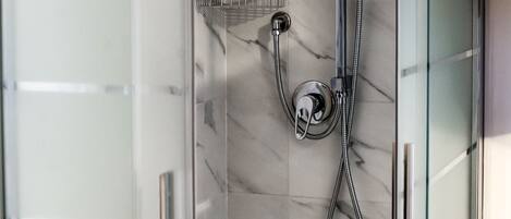 A glass-enclosed shower with a handheld showerhead and a wall-mounted faucet.