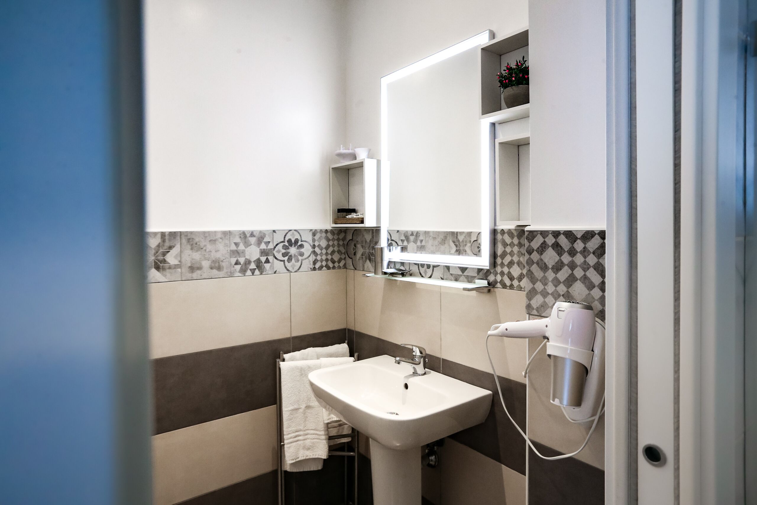 A bathroom with a white sink, a mirror, and a hairdryer mounted on the wall.