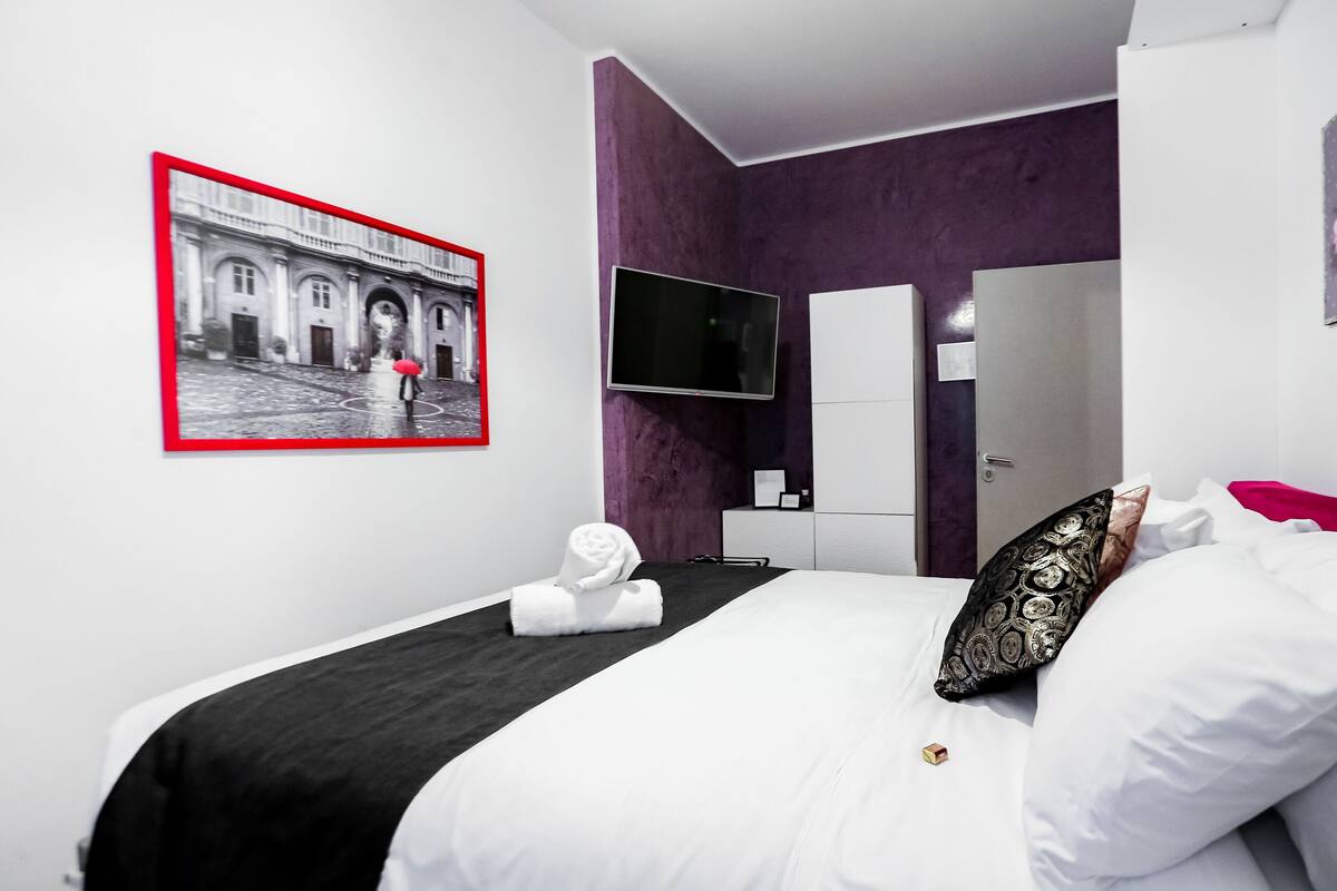 A modern hotel room with a bed, a flat-screen TV, a wardrobe, and a framed picture on the wall.